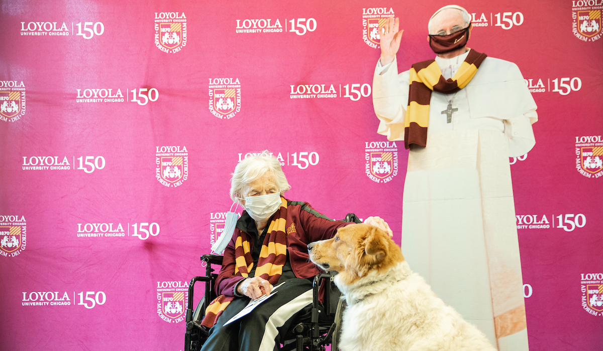 Sister Jean sits near Ashlar the Therapy Dog and a cardboard cut-out of Pope Francis